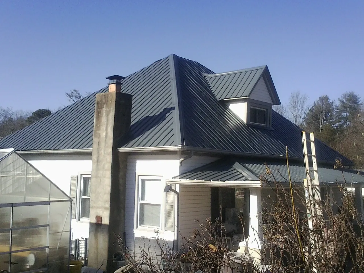 Dark blue standing seam metal roof on a white farmhouse with dormer — Slate & Tile Roof Repair by Roofing Brothers in Reddick