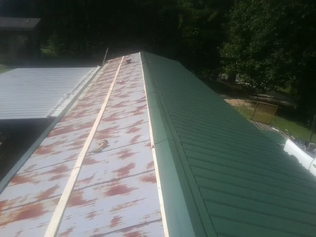 Old rusted panels beside newly installed green metal roofing — Wind Damage Roof Repair by Roofing Brothers in Reddick