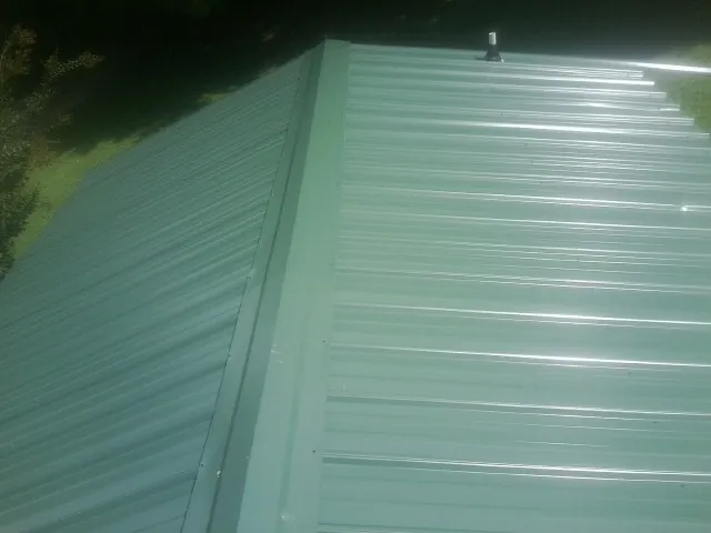 New green metal panels meeting at the ridge of a roof — Flat Roof Repair work by our crew in Reddick